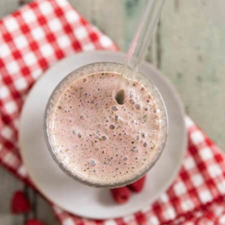 A raspberry yogurt and spinach smoothie in an antique glass with a straw in it.