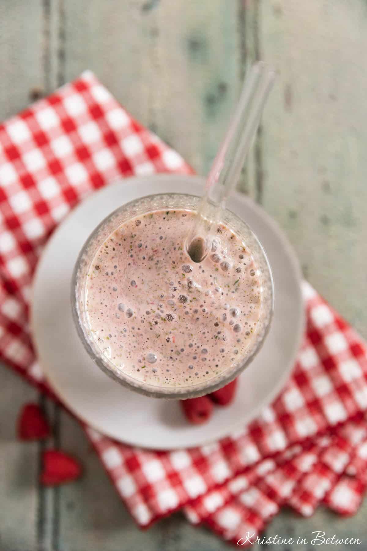 A raspberry yogurt and spinach smoothie in an antique glass with a straw in it.