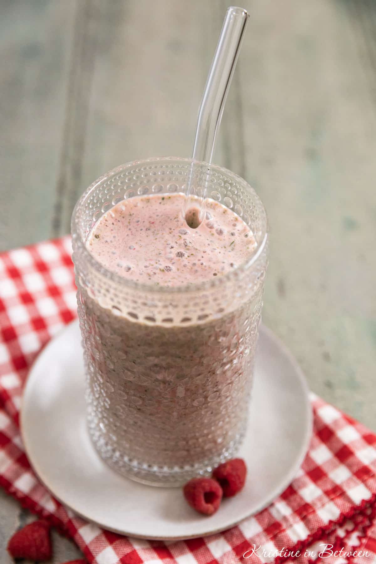A raspberry yogurt and spinach smoothie in an antique glass with a straw in it.
