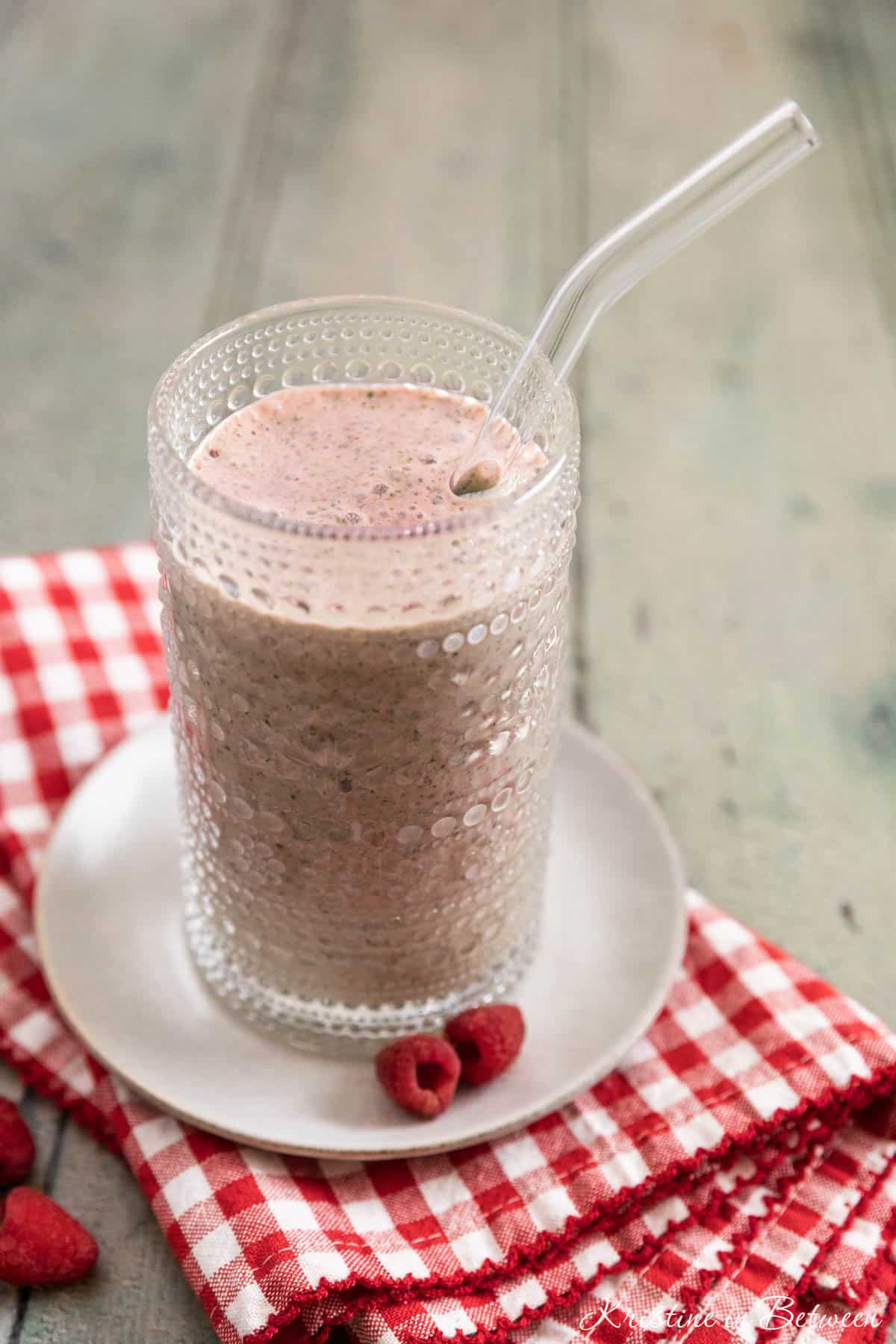 A raspberry yogurt and spinach smoothie in an antique glass with a straw in it.
