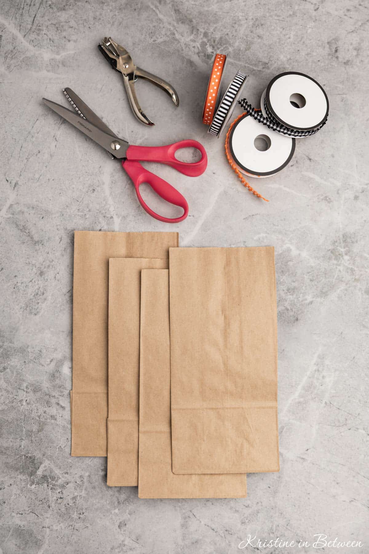 Brown paper bags, scissors, ribbon, and whole punch laid out.