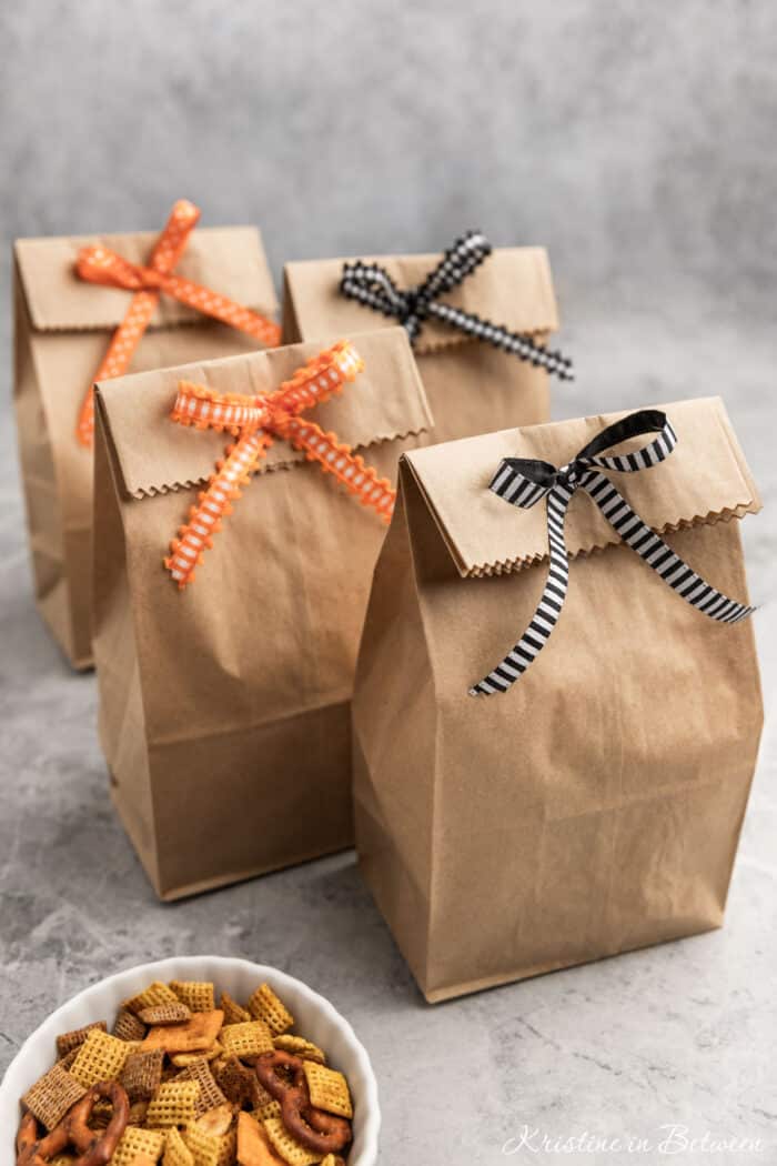 Halloween treat bags made out of brown paper bags sitting with a small bowl of snack mix.