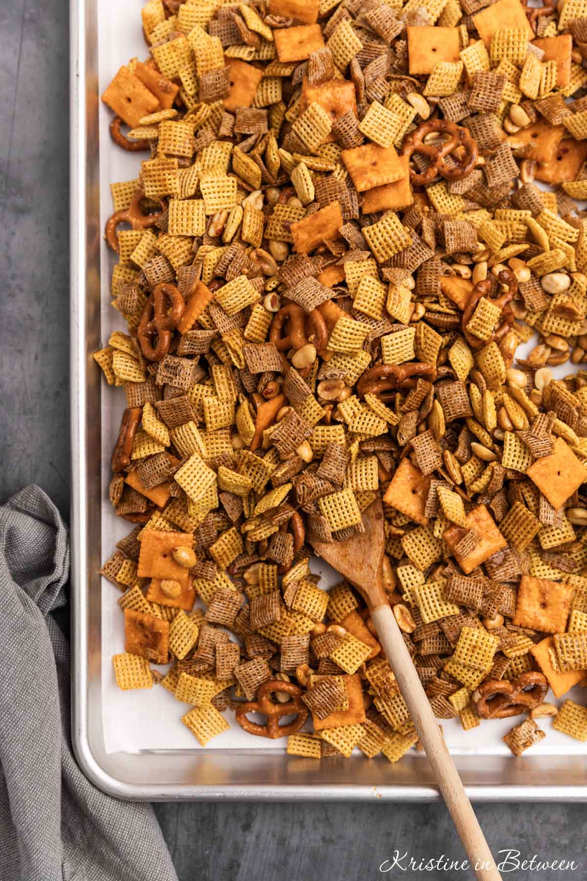 A pan of homemade snack mix ready for baking with a wooden spoon next to it.