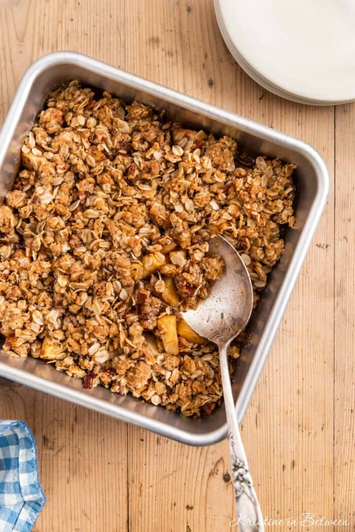 Baked apple crisp in an aluminum baking dish with a spoon in it.