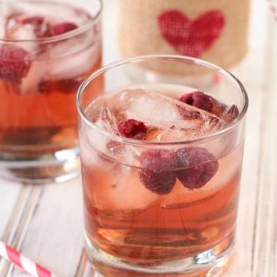 Two cranberry wine spritzers sitting with a red and white striped straw.