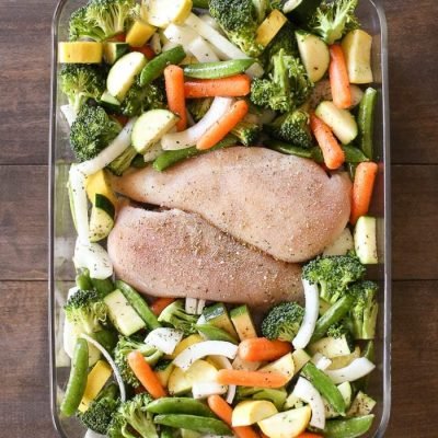 Chicken breasts and chopped veggies laying in a dish ready to bake.
