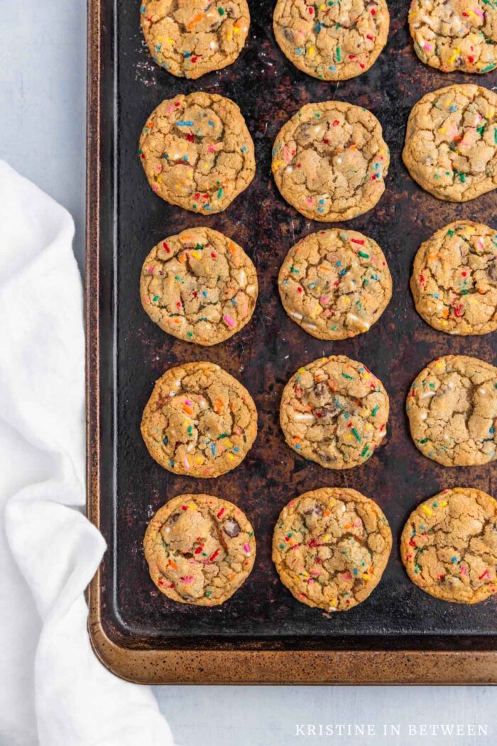 A pan of chocolate chip sprinkle cookies laying on an old cookie sheet with a white napkin.
