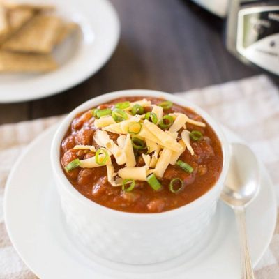 A bowl of chili sitting on a plate with a spoon.