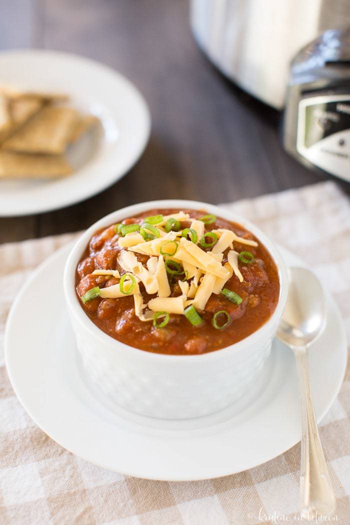 A bowl of chili sitting on a plate with a spoon. 