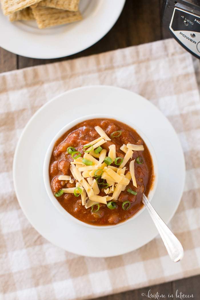 A bowl of chili topped with cheese and green onion.