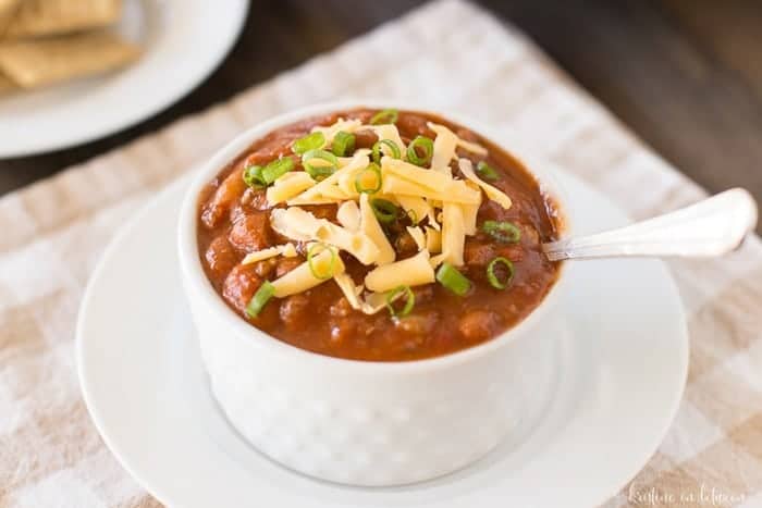 A bowl of chili with a spoon it it, topped with cheese and green onion.
