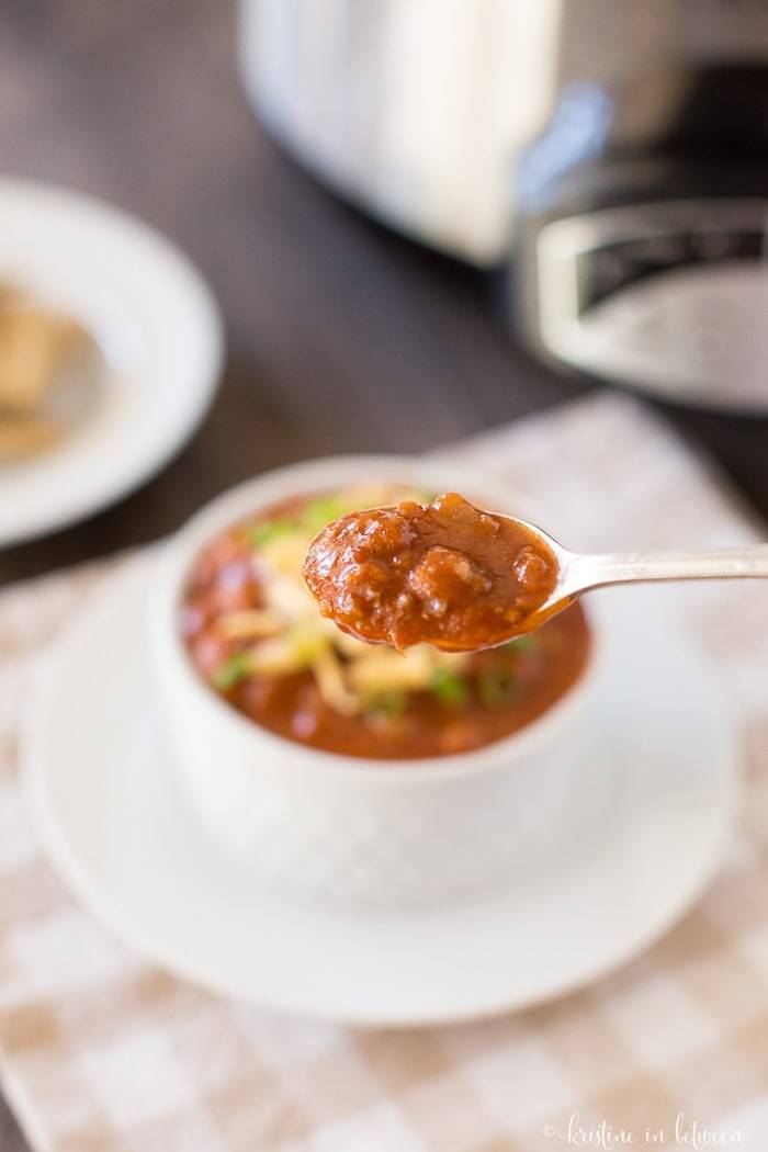 A spoonful of chili with a bowl of chili in the background.