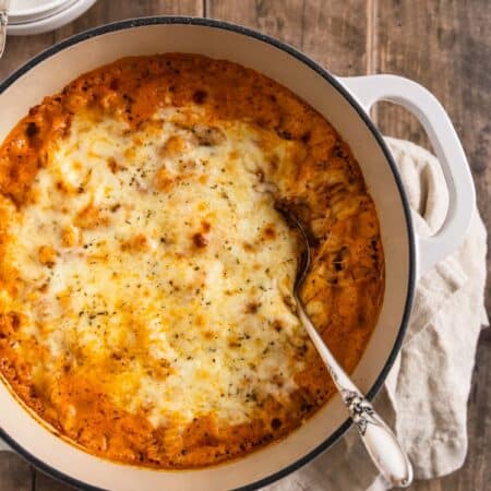Creamy baked ziti in a white dutch oven with two bowls in the background.
