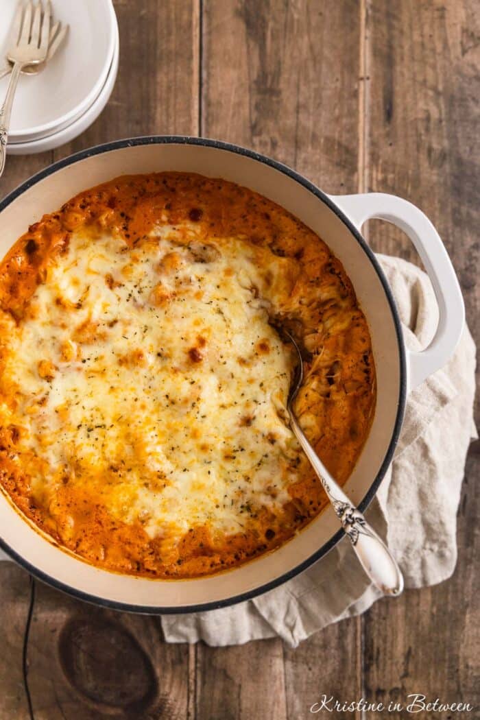 Creamy baked ziti in a white dutch oven with two bowls in the background.