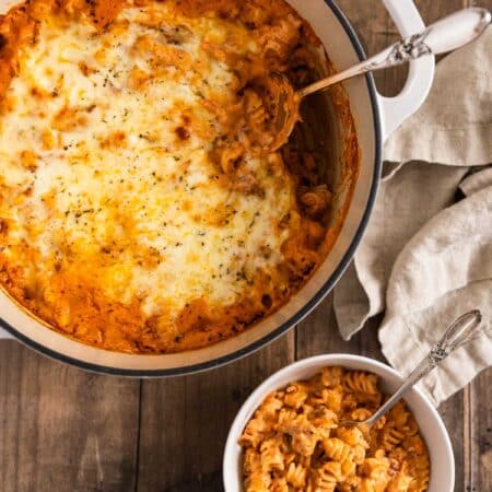 A pot of baked ziti with a bowl of dished up sitting next to it.