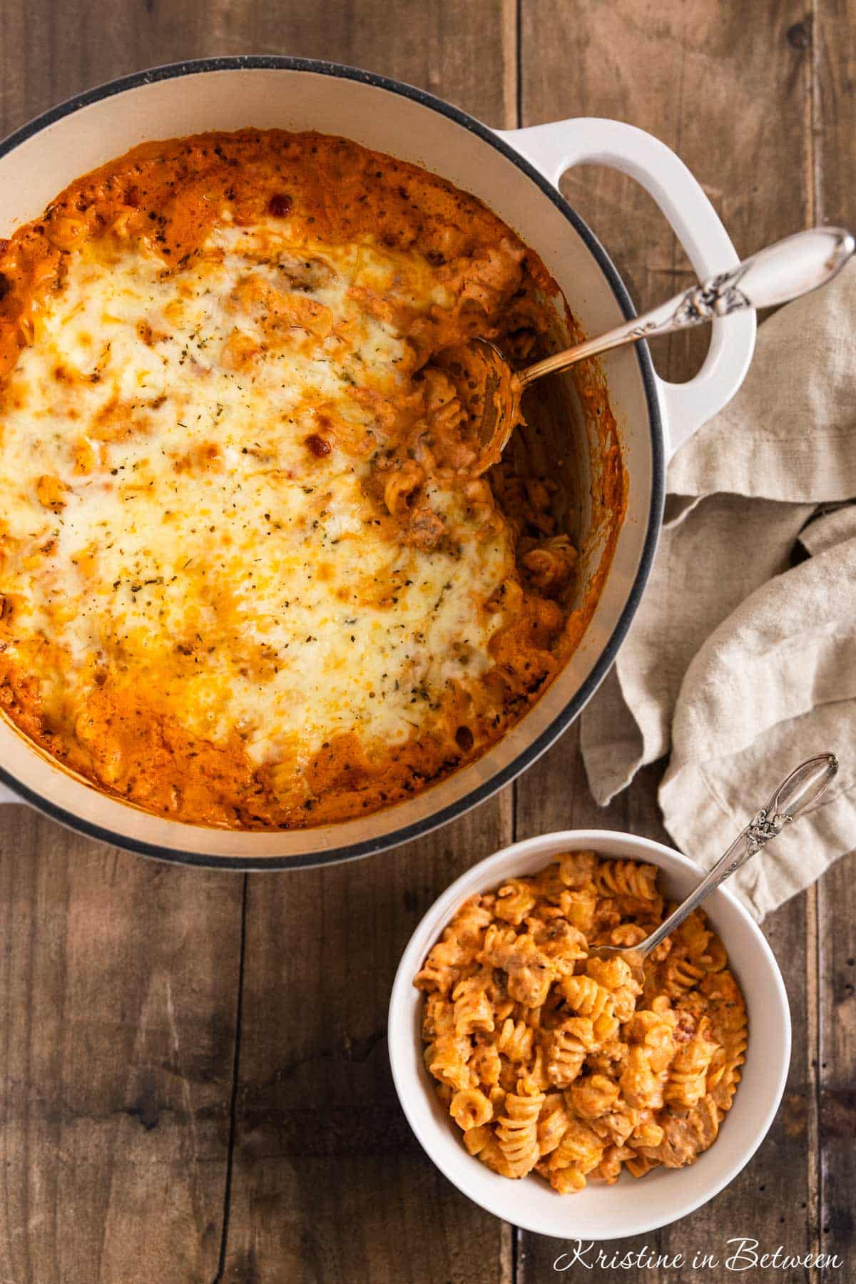 A pot of baked ziti with a bowl of dished up sitting next to it.