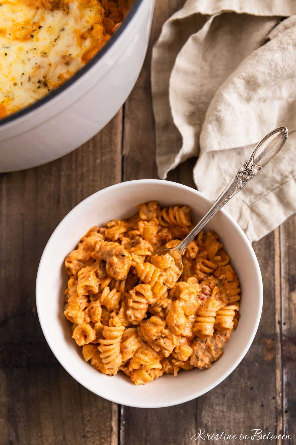 Baked ziti in a white bowl with a fork in it and a tan napkin.