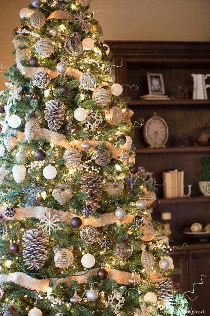 A fully decorated Christmas tree with neutral colored ornaments and burlap ribbon.