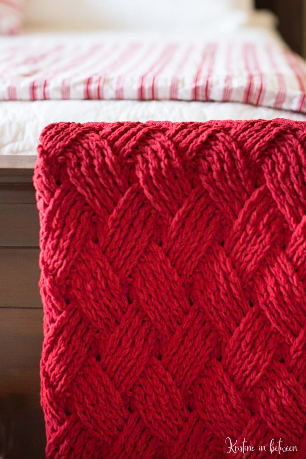 A red crocheted blanket fold on the end of a wooden bed.