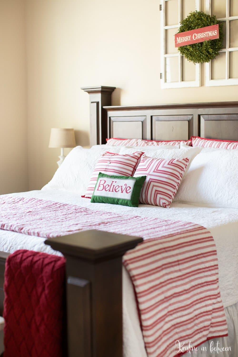 A wooden bed with read and white bedding and a wreath with a Merry Christmas sign hanging above it.