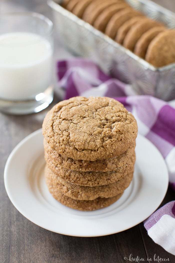 A stack of cookies on a white plate with a glass of milk in the background.