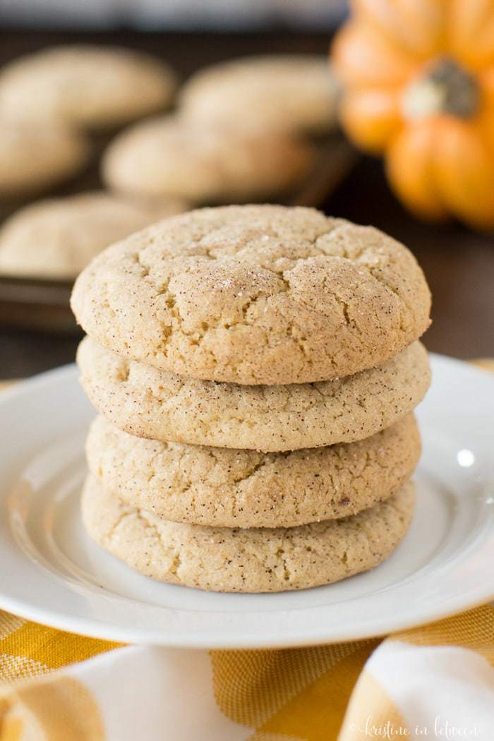 Pumpkin snickerdoodle cookies stacked up on a plate with a pumpkin in the background.