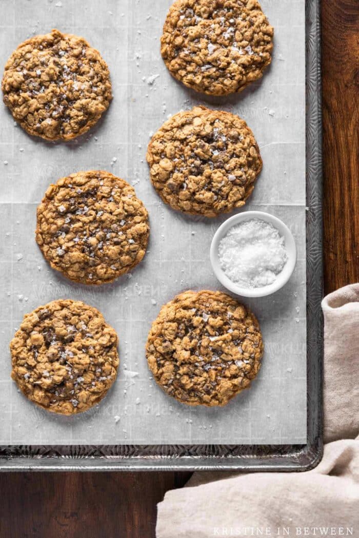 Oatmeal cookies on a baking sheet with sea salt sprinkled on top.