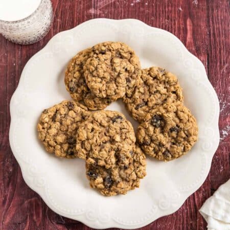 Old-fashioned oatmeal raisin cookies stacked upon a white plate with one broken in half to show the inside.