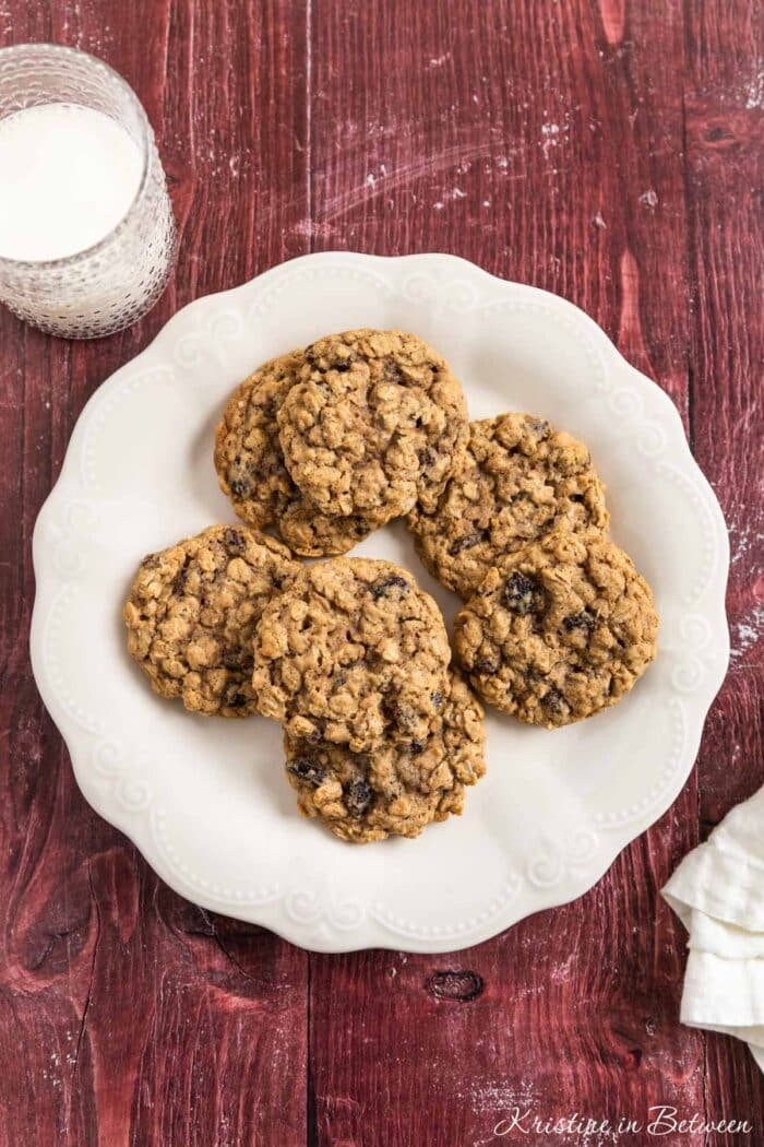 Old-fashioned oatmeal raisin cookies stacked upon a white plate with one broken in half to show the inside.