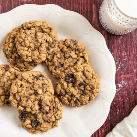 Old-fashioned oatmeal raisin cookies stacked upon a white plate with one broken in half to show the inside.