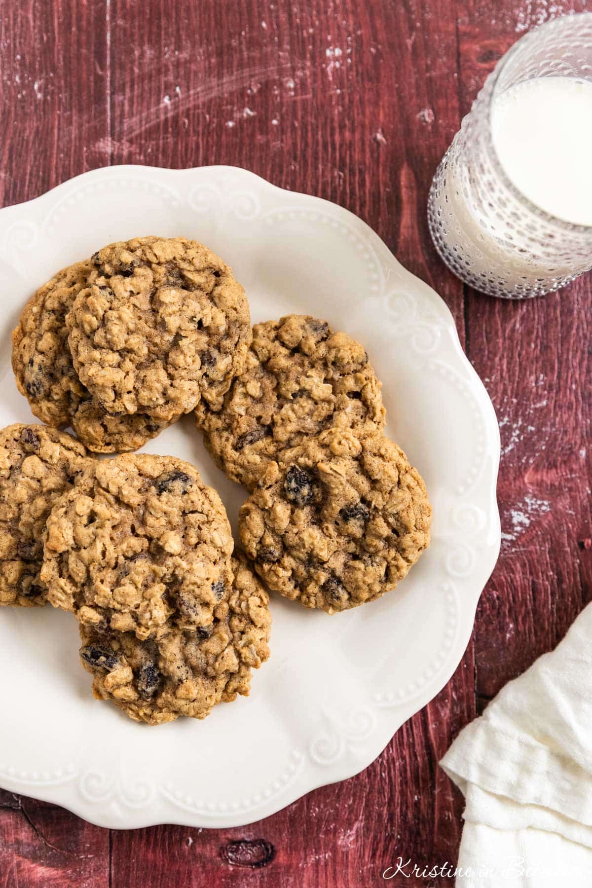 Old-fashioned oatmeal raisin cookies stacked upon a white plate with one broken in half to show the inside.
