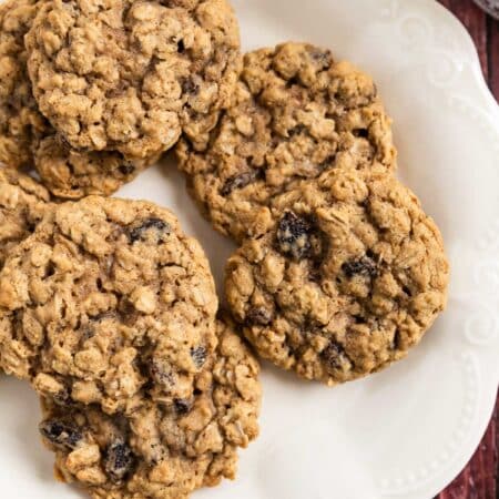 Old-fashioned oatmeal raisin cookies stacked upon a white plate with one broken in half to show the inside.