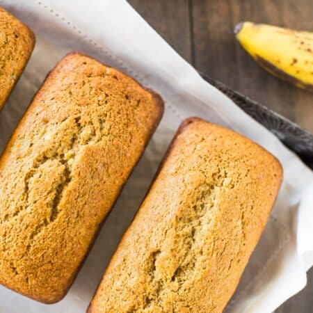 Three loaves of banana bread sitting on a baking tray with a white napkin.