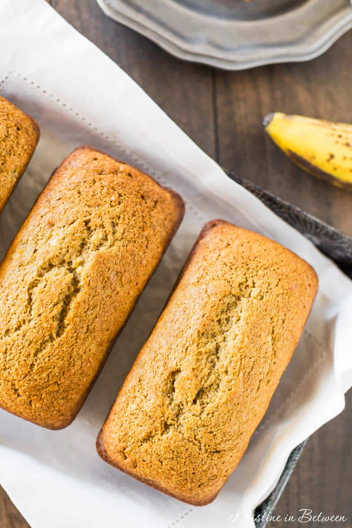 Three loaves of banana bread sitting on a baking tray with a white napkin.