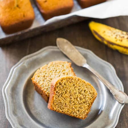 Two slices of banana bread on a metal plate with an antique butter knife.