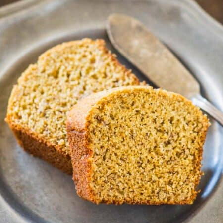Two slices of banana bread on a metal plate with an antique butter knife.