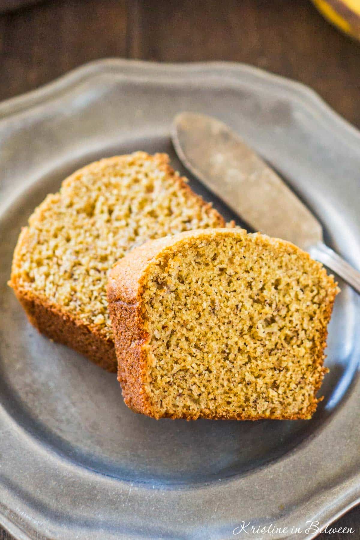 Two slices of banana bread on a metal plate with an antique butter knife.