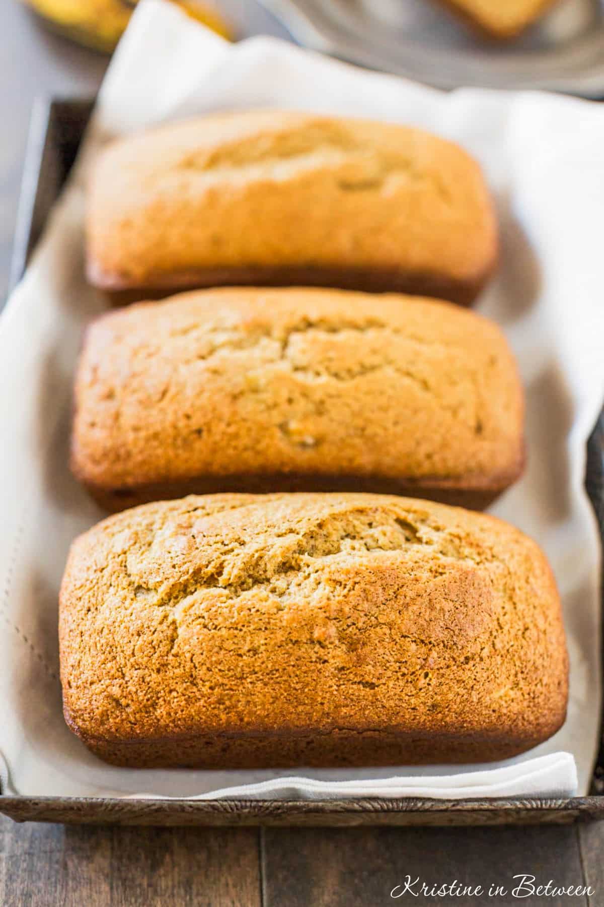 Three loaves of banana bread sitting on a baking tray with a white napkin.