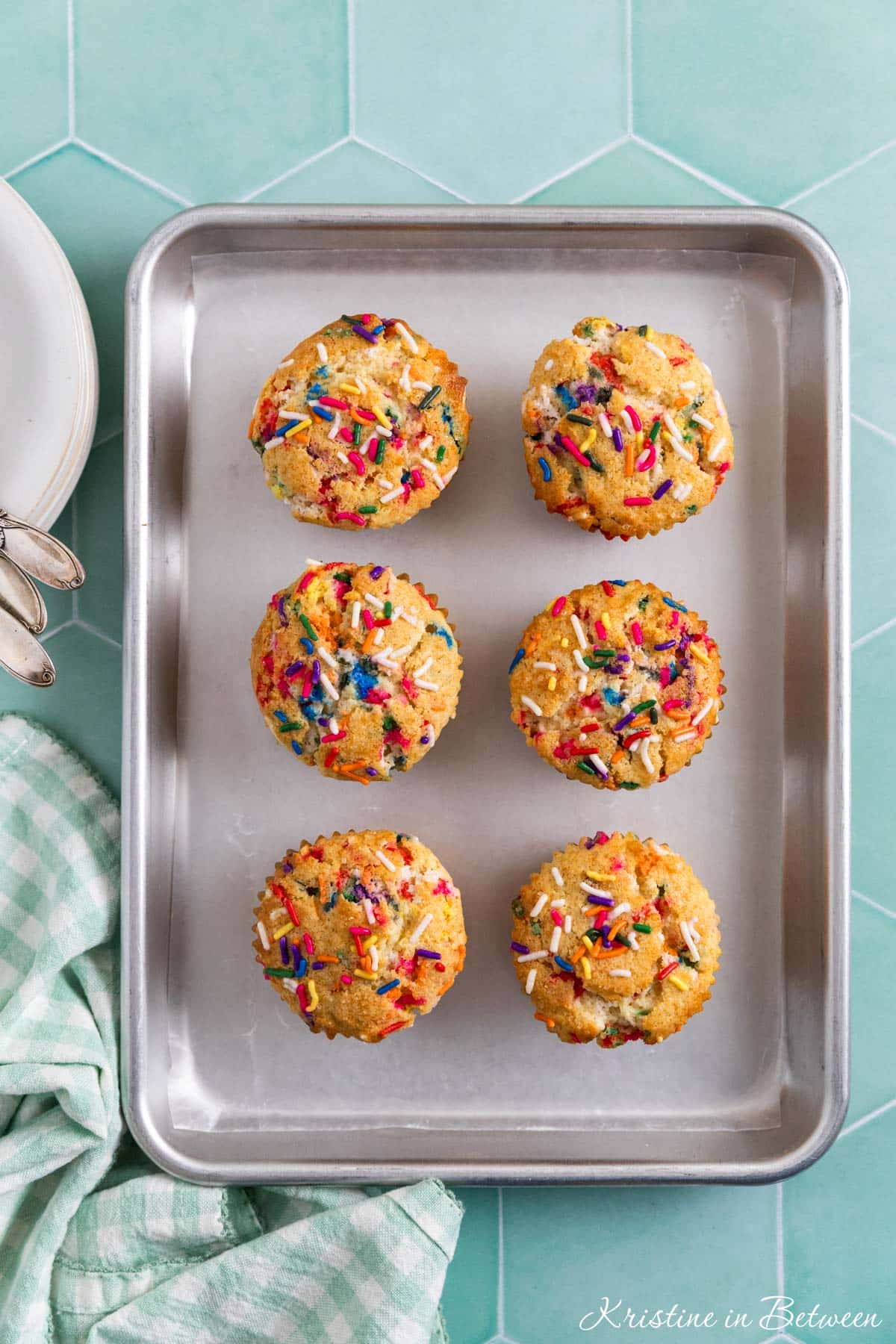 Birthday cake muffins on a baking tray with a napkin sitting next to them.