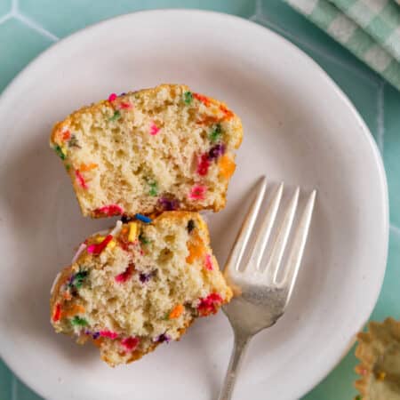A birthday cake muffin cut in half with a fork sitting next to it.