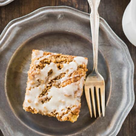 A slice of banana crumb cake on a metal plate with an antique fork.