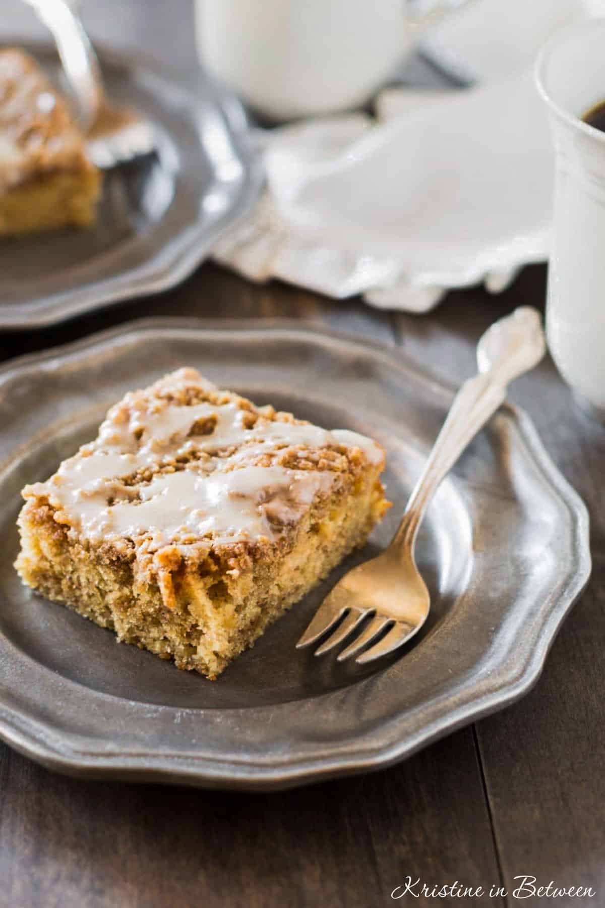 A slice of banana crumb cake on a metal plate with an antique fork.