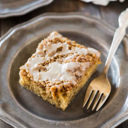 A slice of banana crumb cake on a metal plate with an antique fork.