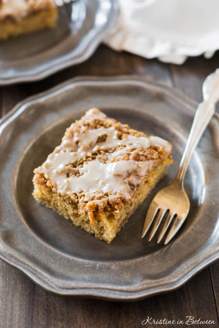 A slice of banana crumb cake on a metal plate with an antique fork.