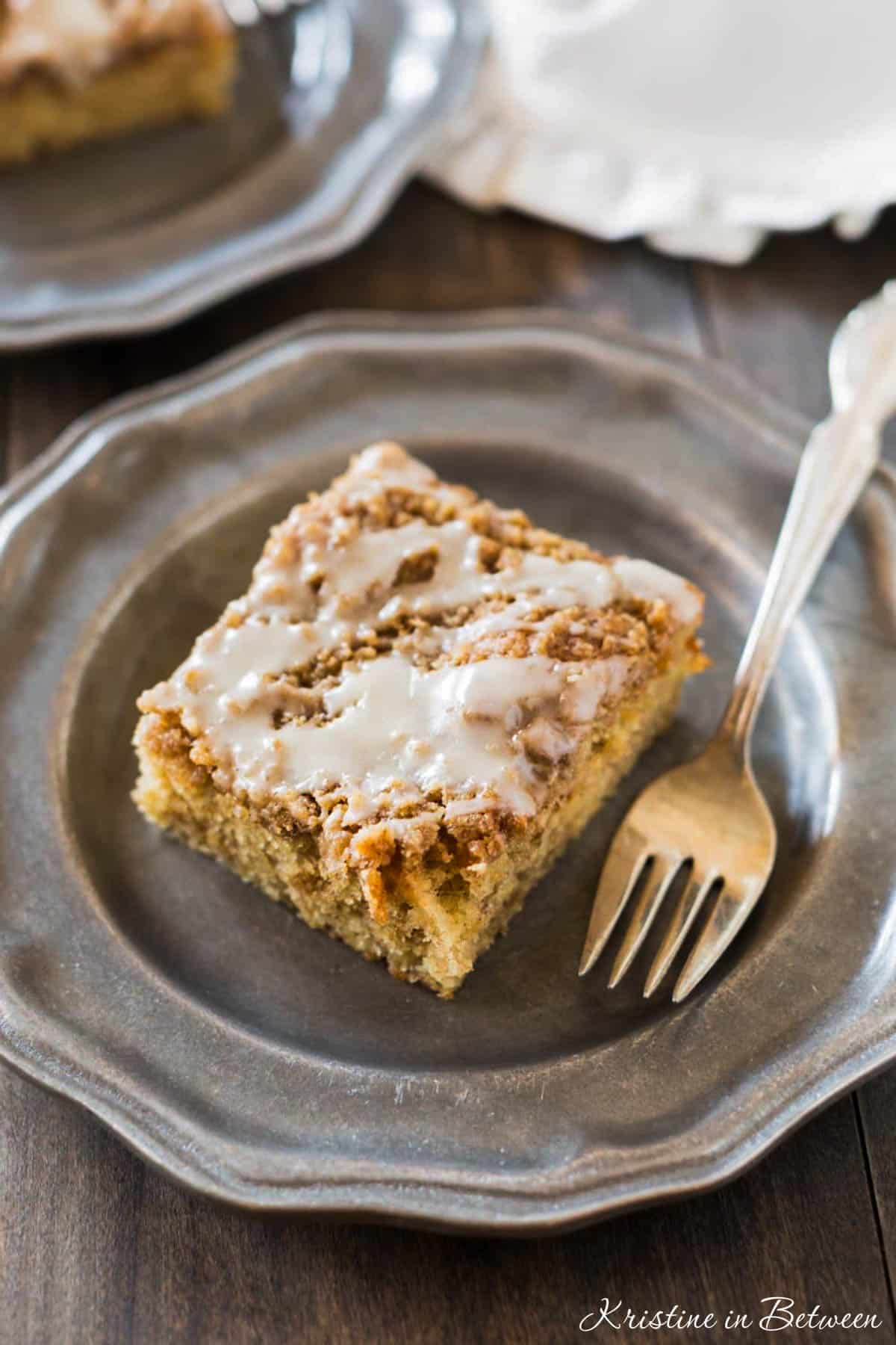 A slice of banana crumb cake on a metal plate with an antique fork.