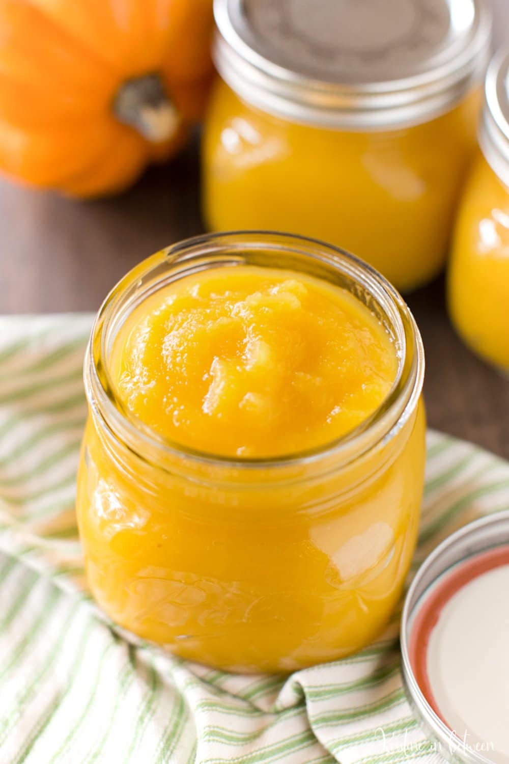 A jar of pumpkin puree sitting on a table with a sugar pumpkin and a few jars of puree.