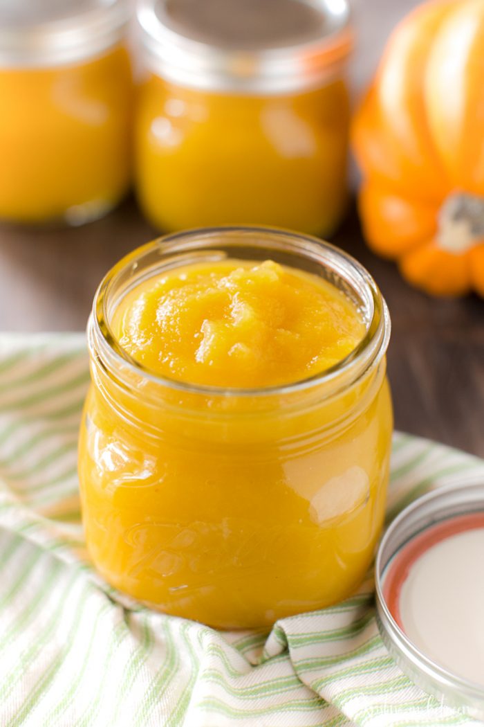 A jar of pumpkin puree sitting on a table with a sugar pumpkin.