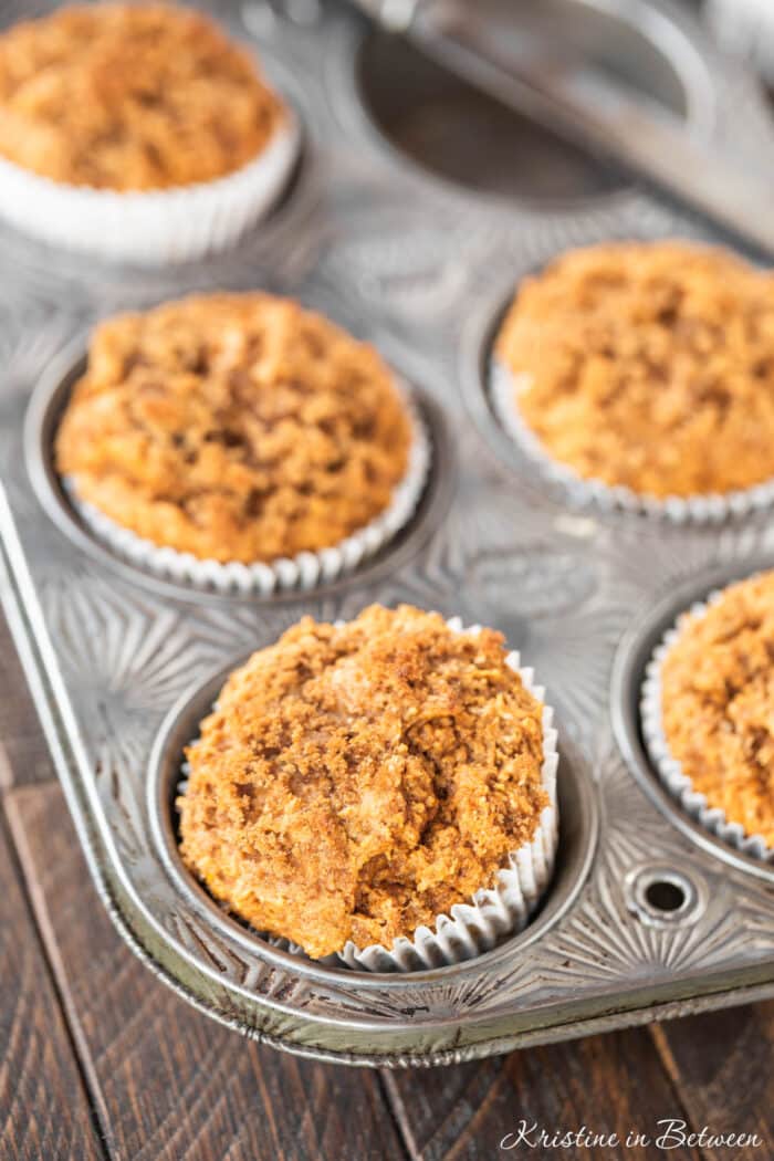 Pumpkin muffins with a crumb topping in a muffin tin with a knife sitting next to them.