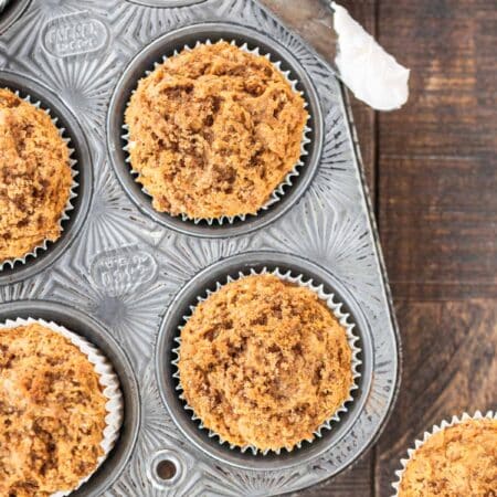 Pumpkin muffins with a crumb topping in a muffin tin with a knife sitting next to them.