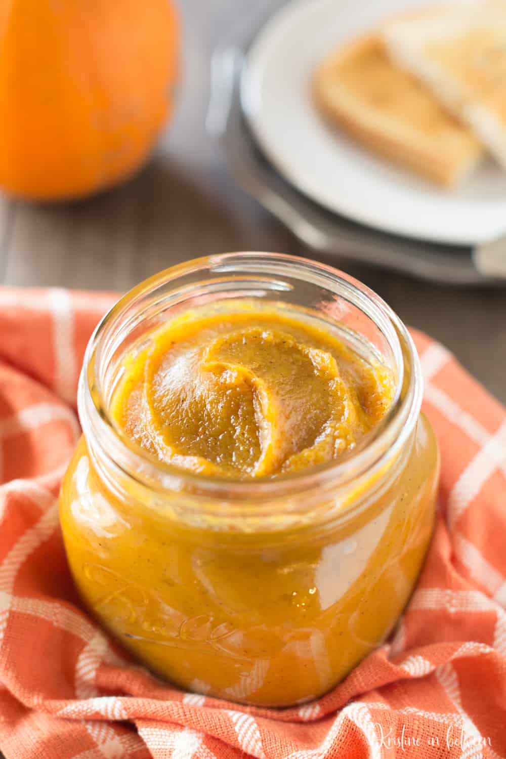 A jar of pumpkin butter sitting on a table with a sugar pumpkin.